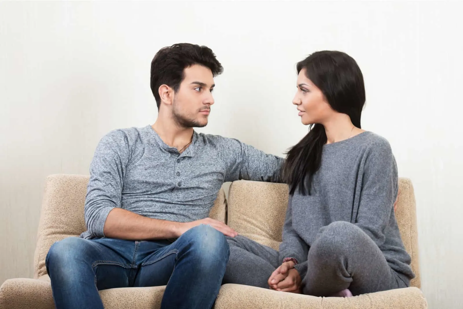 זוג שמח צעיר מדבר יחד יושב על ספה