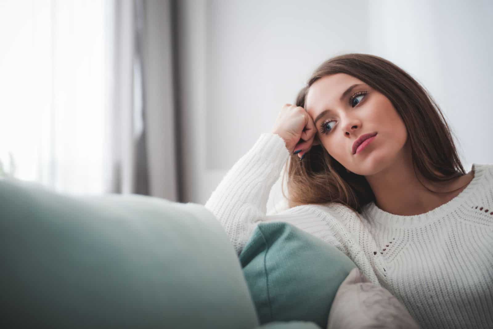 a woman with long brown hair sits on the couch in thought
