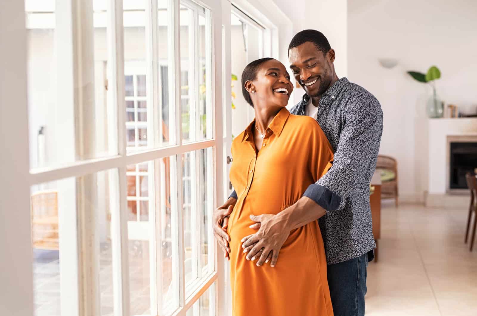 a couple having a baby standing by a window