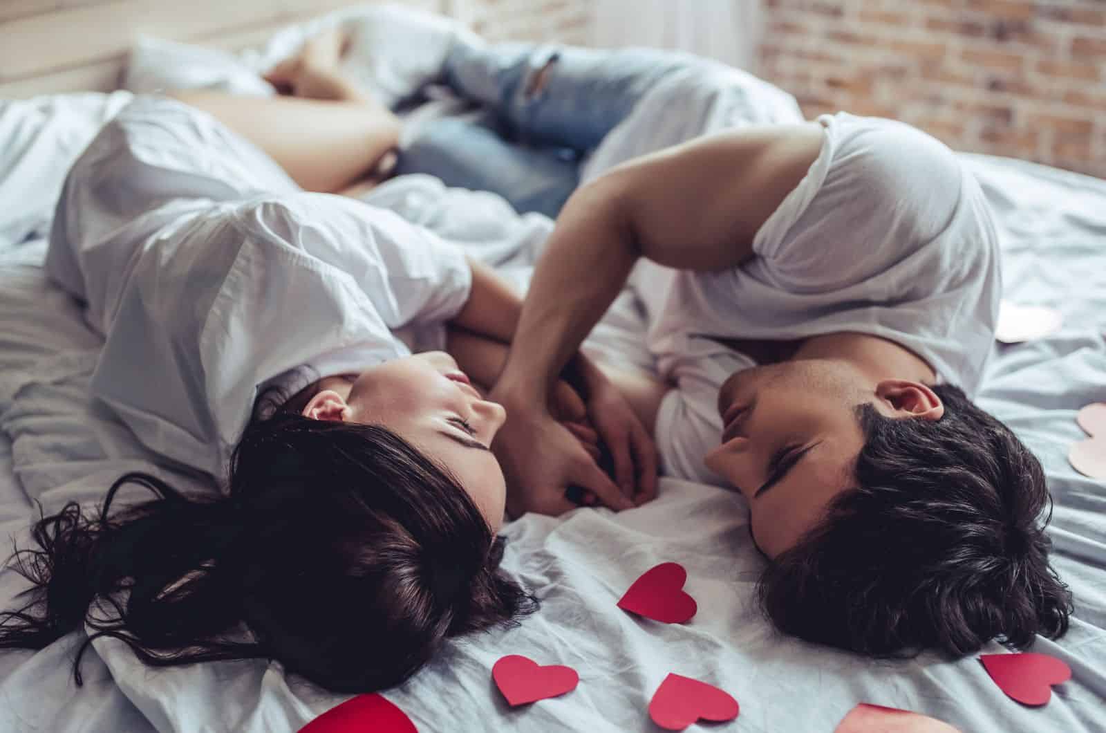 couple lying in bed together with red paper hearts and looking at each other