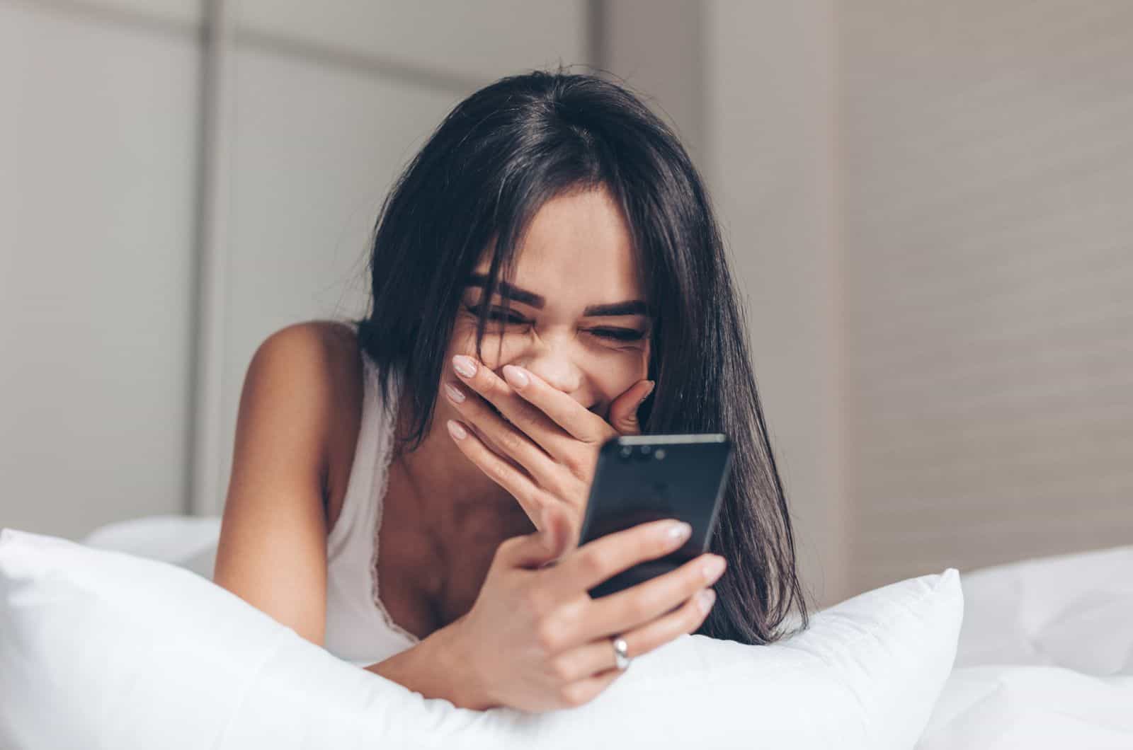 girl laughing and staring at her phone while lying on bed