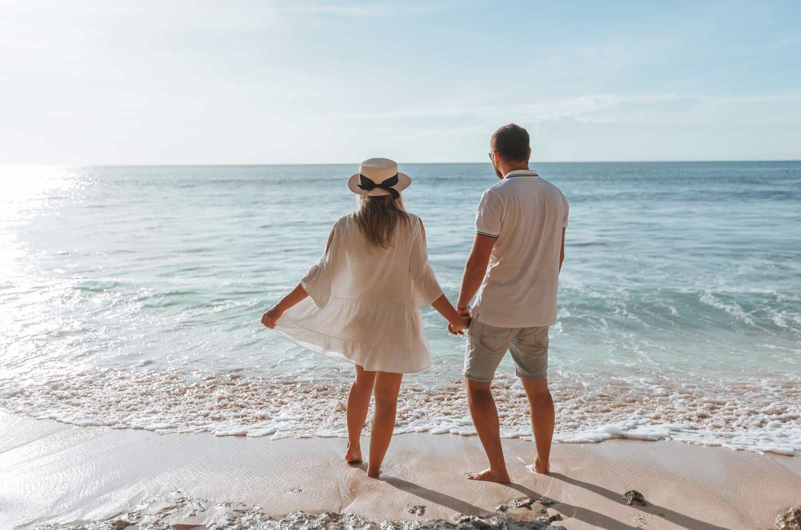 un hombre y una chica se cogen de la mano y contemplan la puesta de sol en la playa