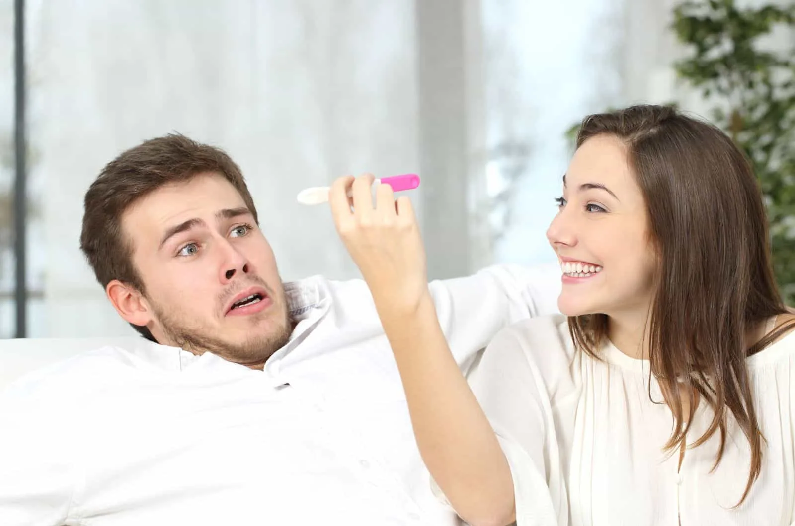 woman laughing and showing scared man a fake pregnancy test