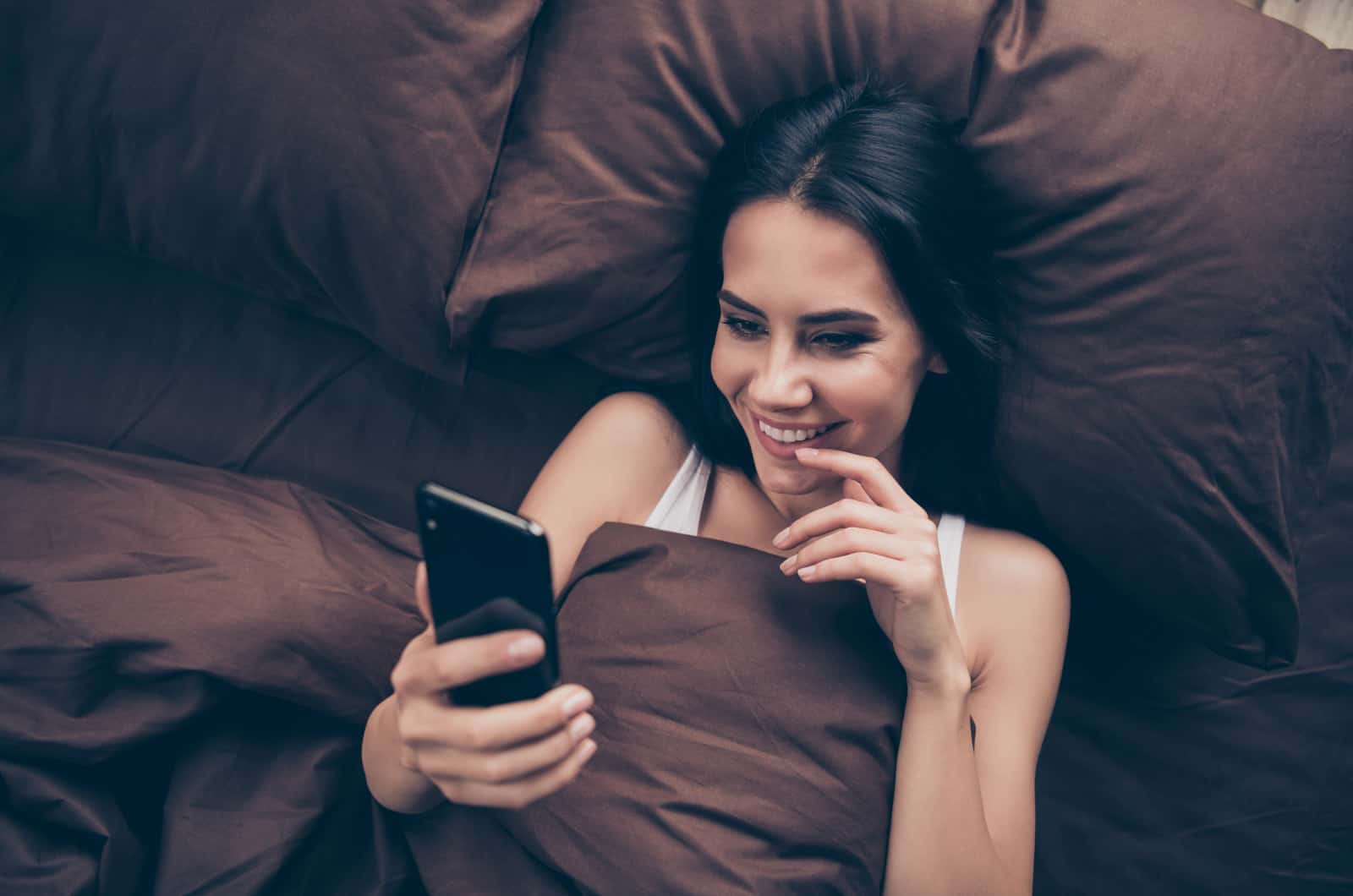 donna sdraiata a letto che risponde a sms flirtanti