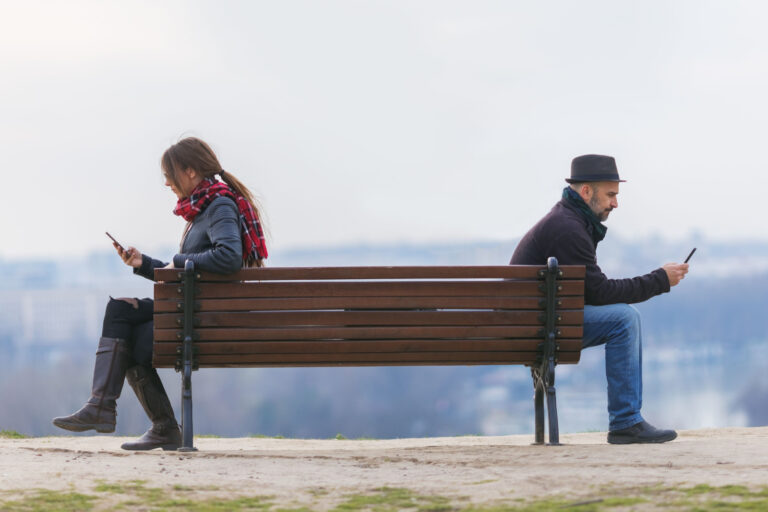 homem e mulher sentam-se separados num banco de jardim
