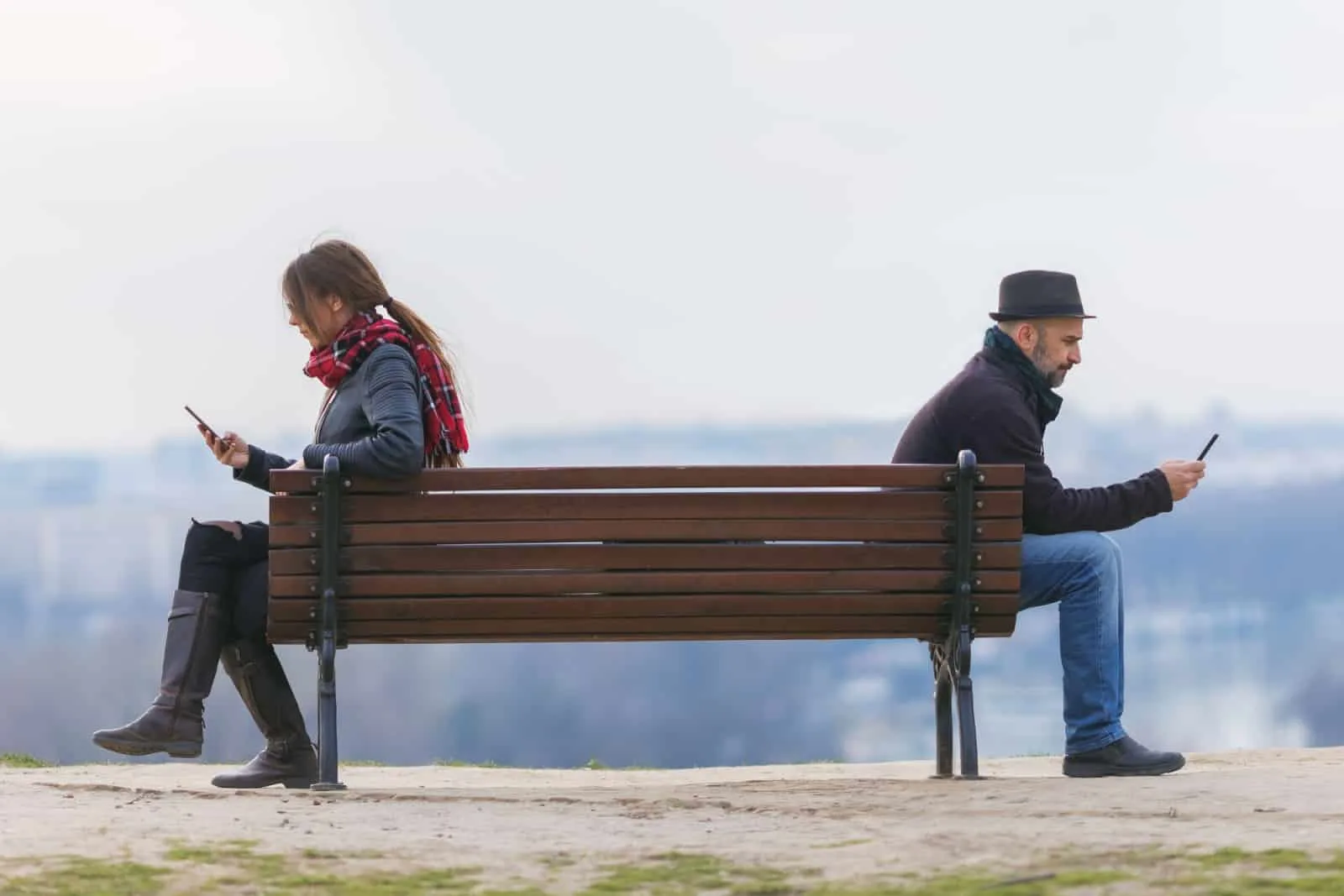 man and woman sit apart on a park bench