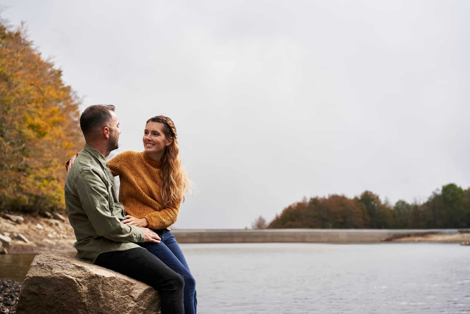 man and woman having a conversation while sitting on a rock beside a lake in nature