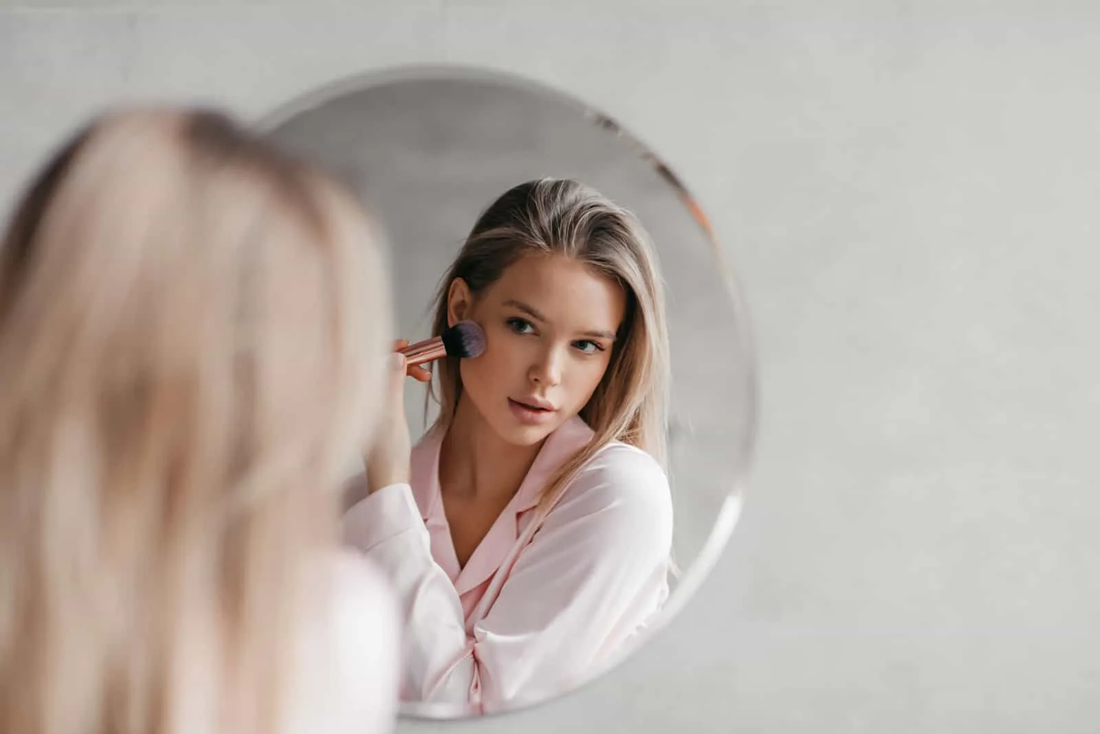 Beautiful woman in pajamas in front of mirror, holding brush and applying makeup