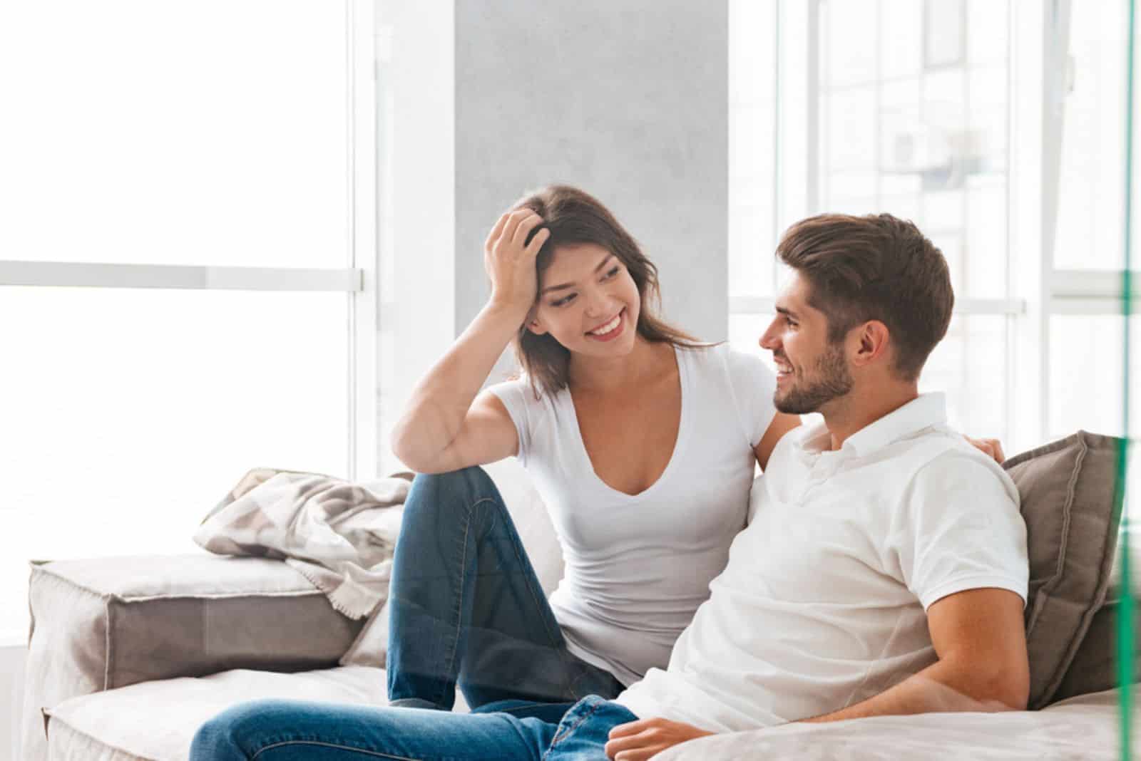 Cheerful beautiful young couple sitting and talking on sofa at home