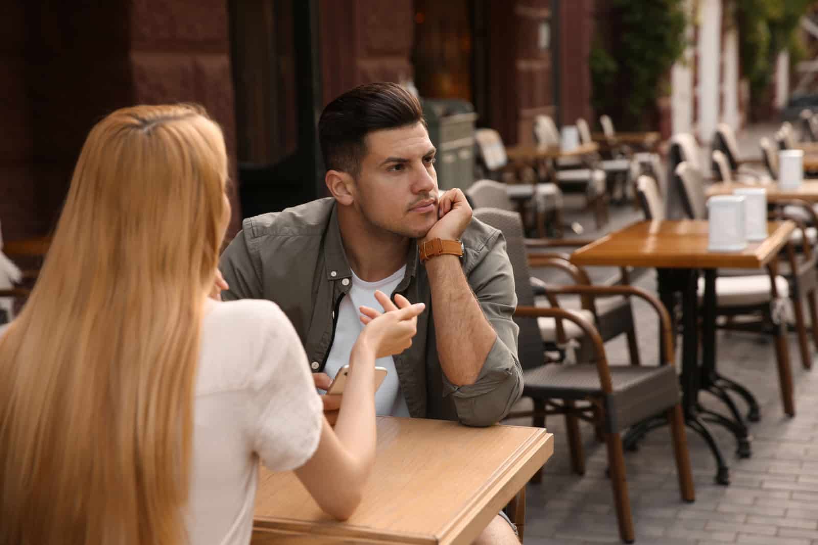 Uomo che si annoia durante il primo appuntamento con una giovane donna troppo loquace in un caffè all'aperto