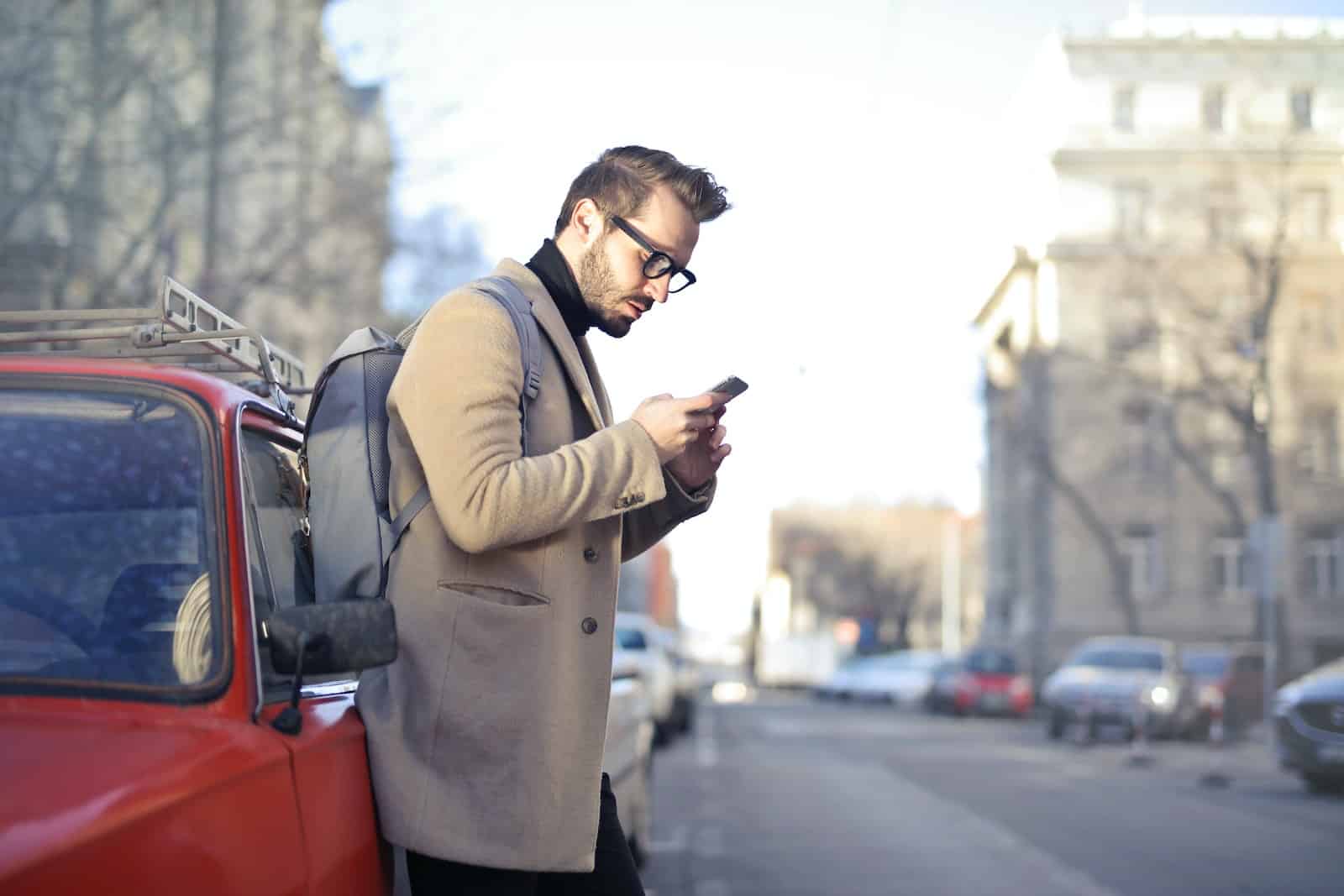 uomo in cappotto beige con telefono in mano