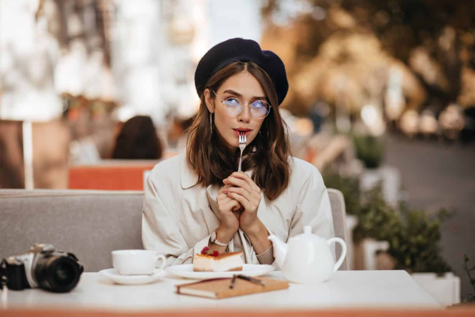 una hermosa mujer con un sombrero en la cabeza está sentada a la mesa y comiendo