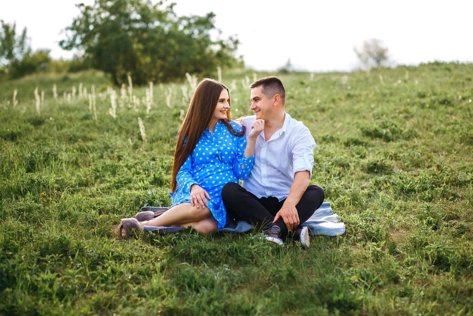 una donna incinta sorridente siede sull'erba con un uomo