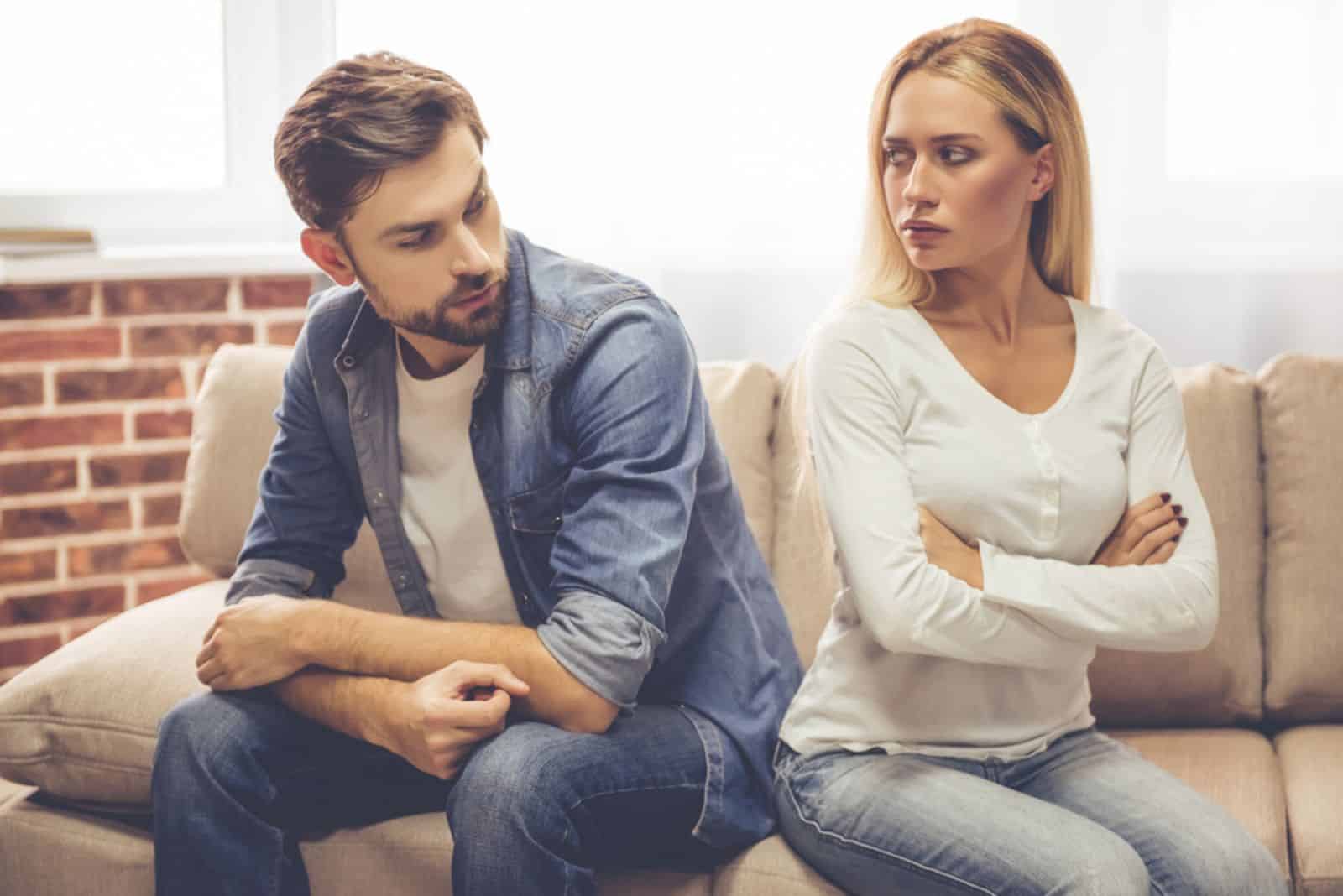 couple is sitting back to back on the couch and looking offended at each other