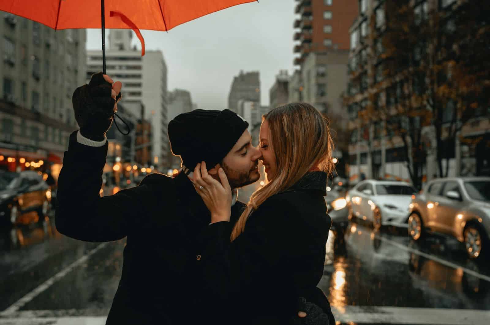 casal a beijar-se enquanto o homem segura um guarda-chuva