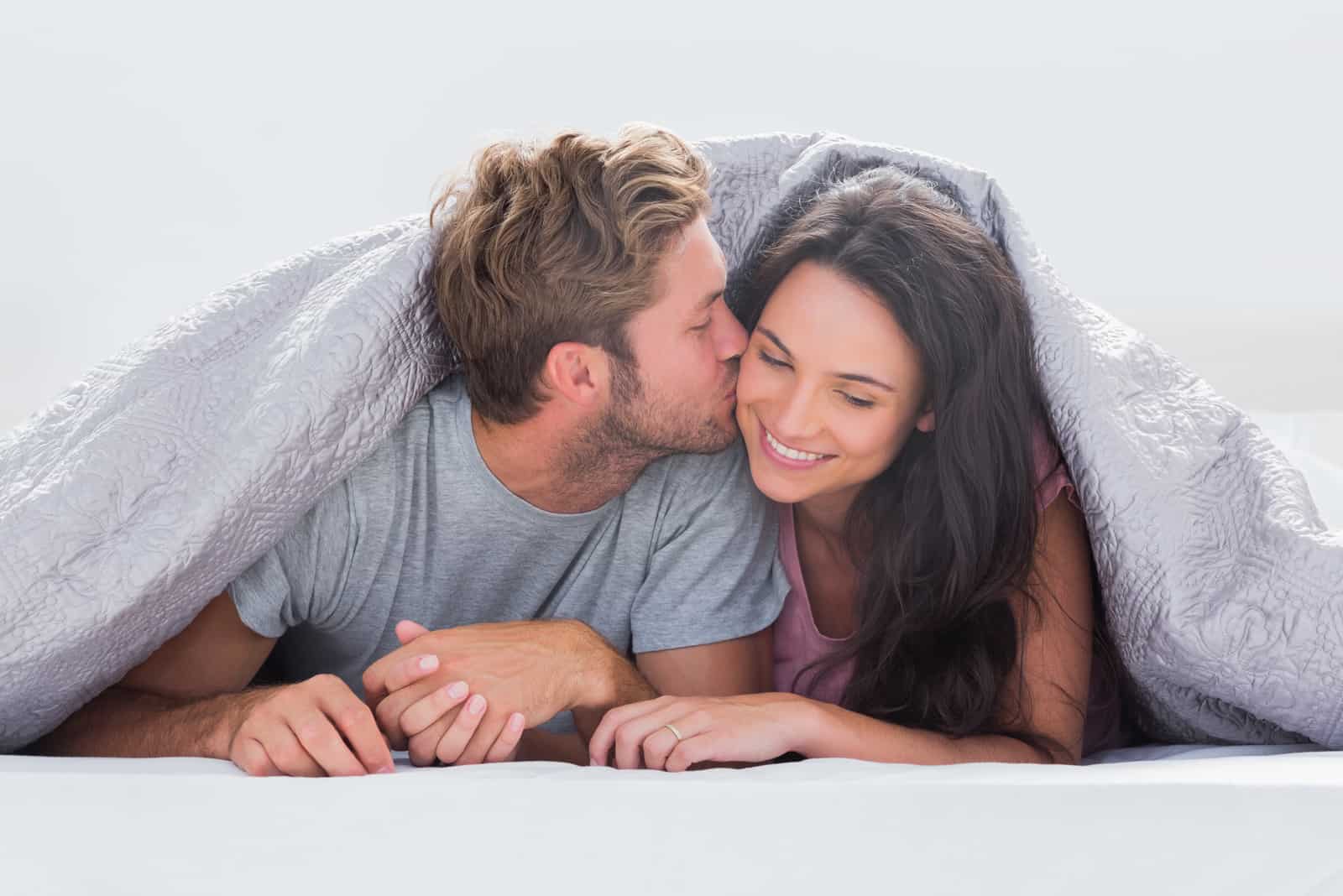 homem beija mulher debaixo de um edredão