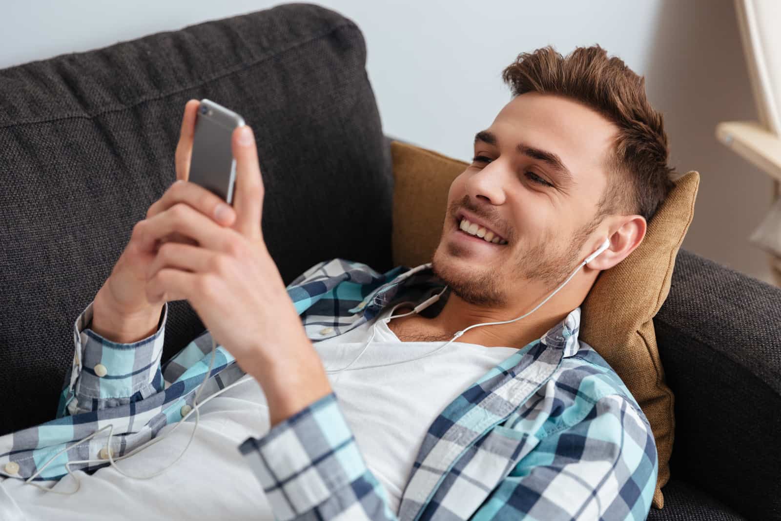 man lying on couch and looking at phone