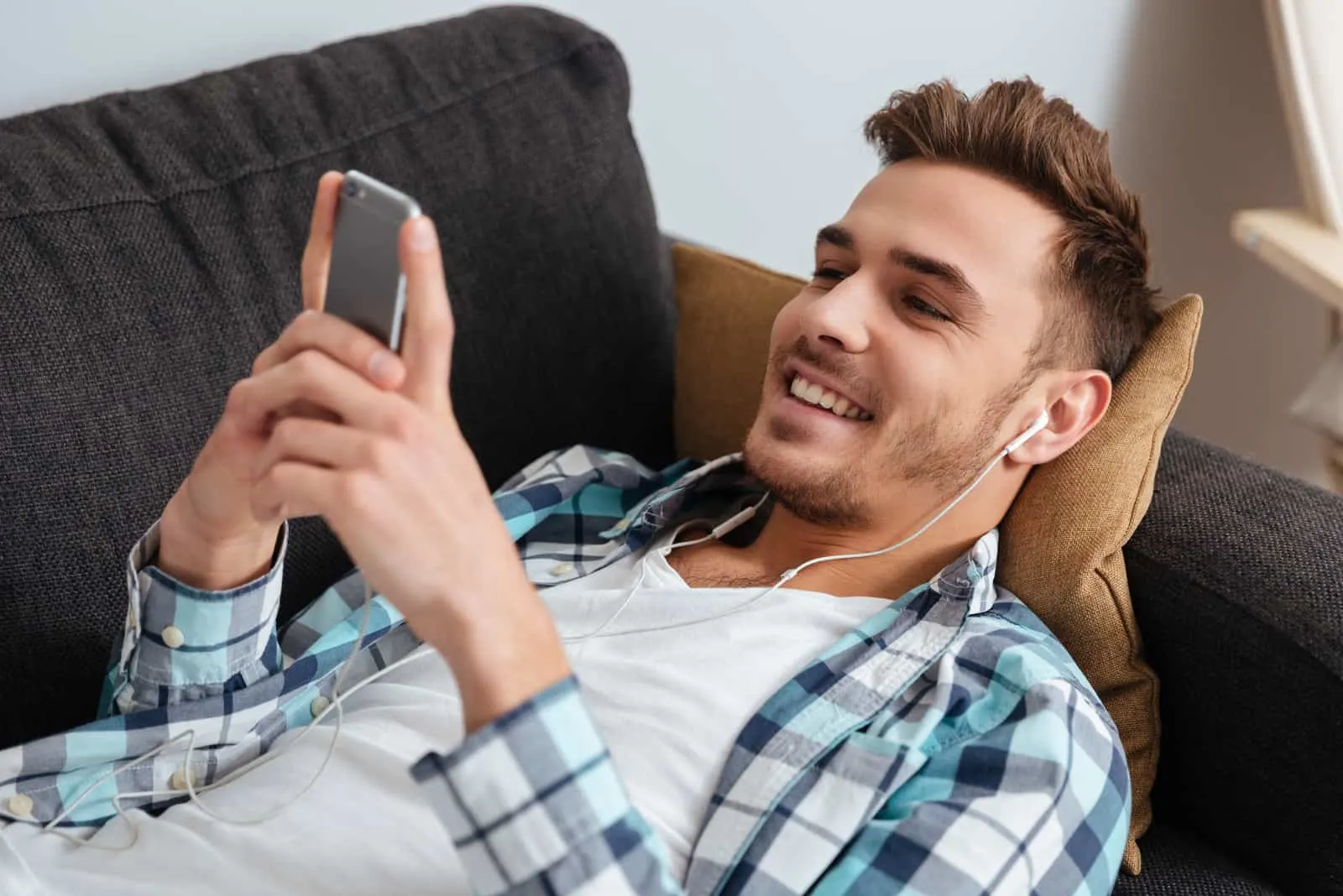 man lying on couch and looking at phone