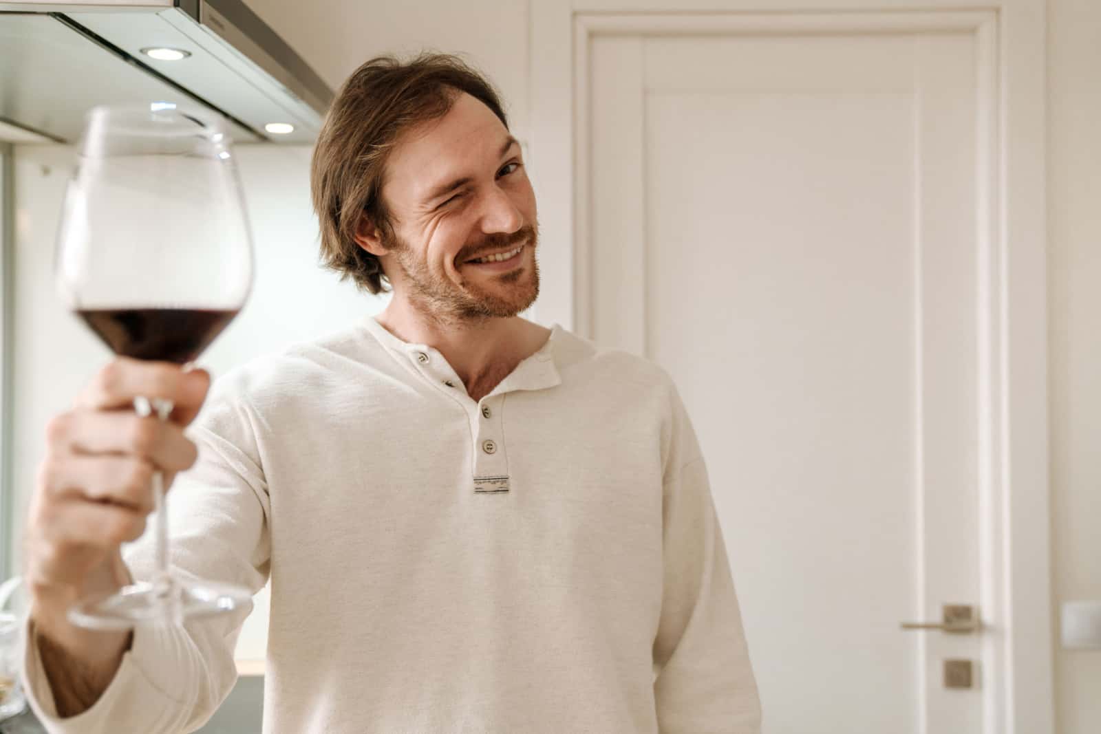 man smiling and winking while drinking wine in kitchen at home