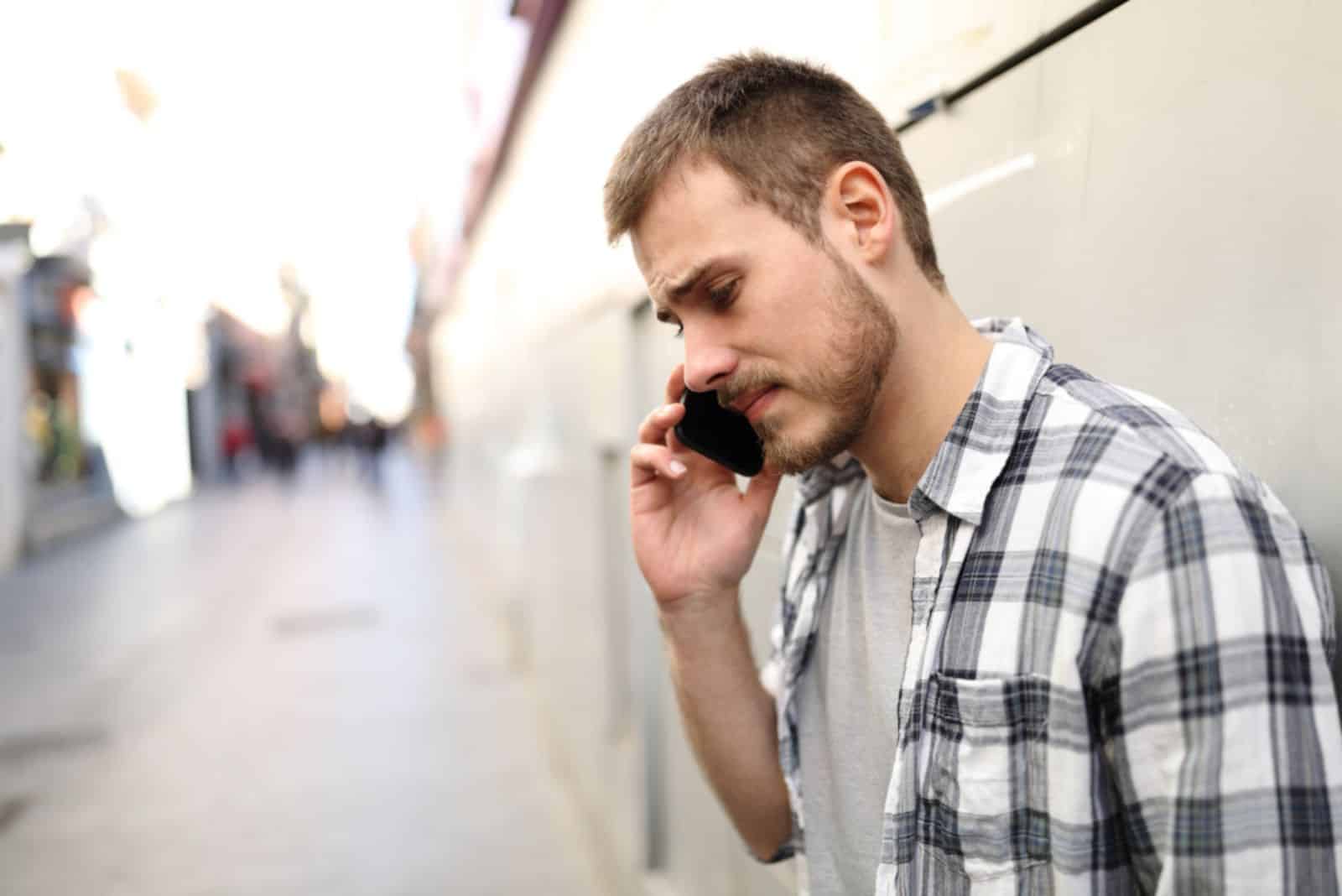 sad man talking on phone alone in a solitary street