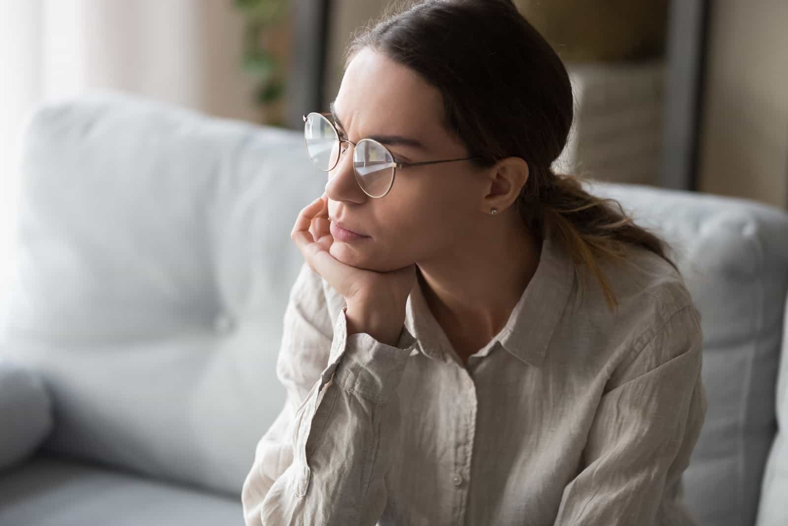 mujer seria con gafas sentada sumida en profundos pensamientos