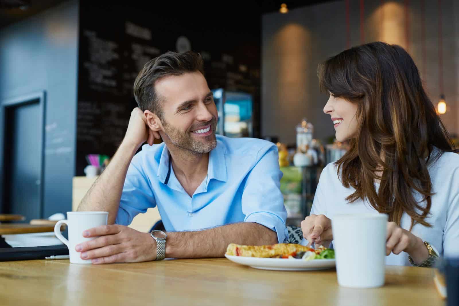 pareja sonriente y cariñosa sentada en un café y hablando