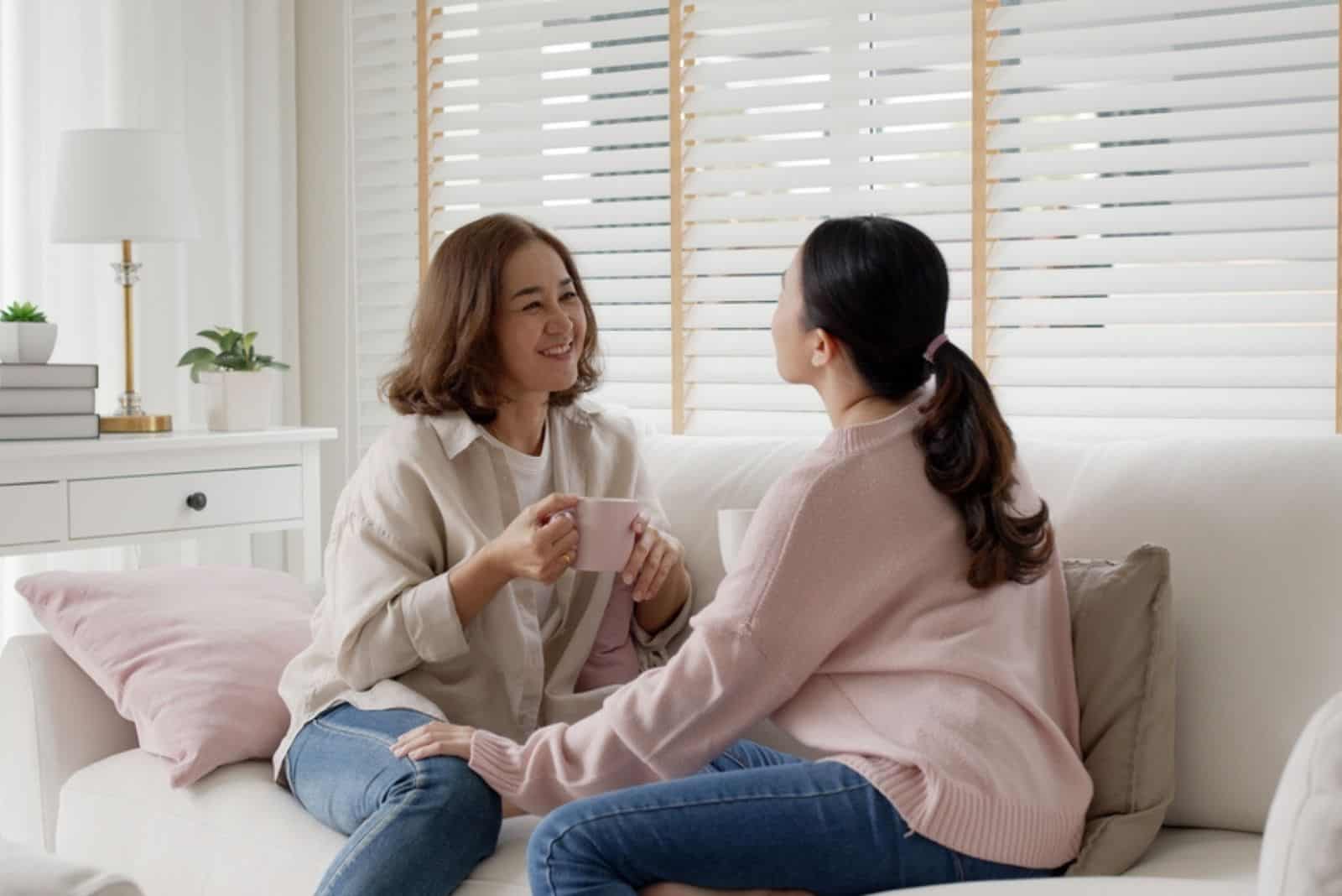 two women are sitting on the couch and talking