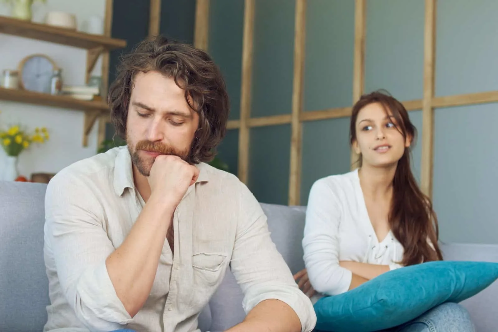 a beautiful girl with long black hair is sitting on the couch next to a man who has turned his back to her