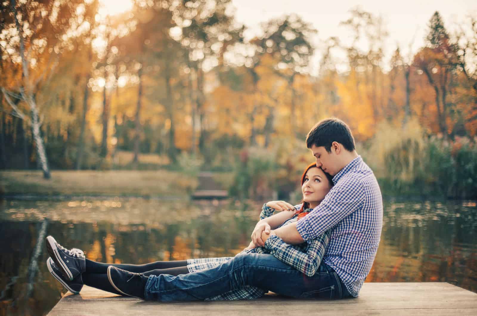 couple sitting together at the deck in front of a lake