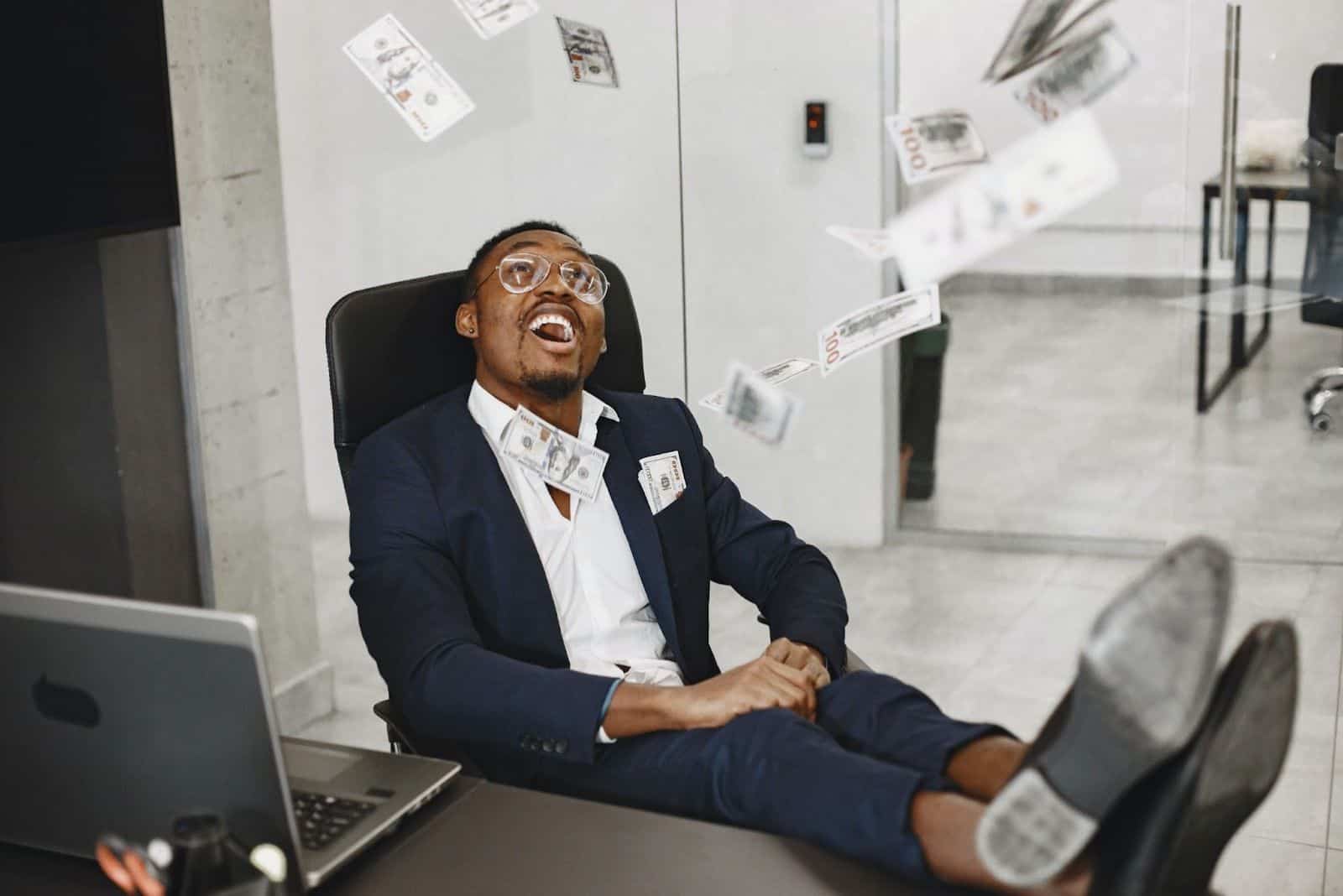 happy business man sitting in office with flying money