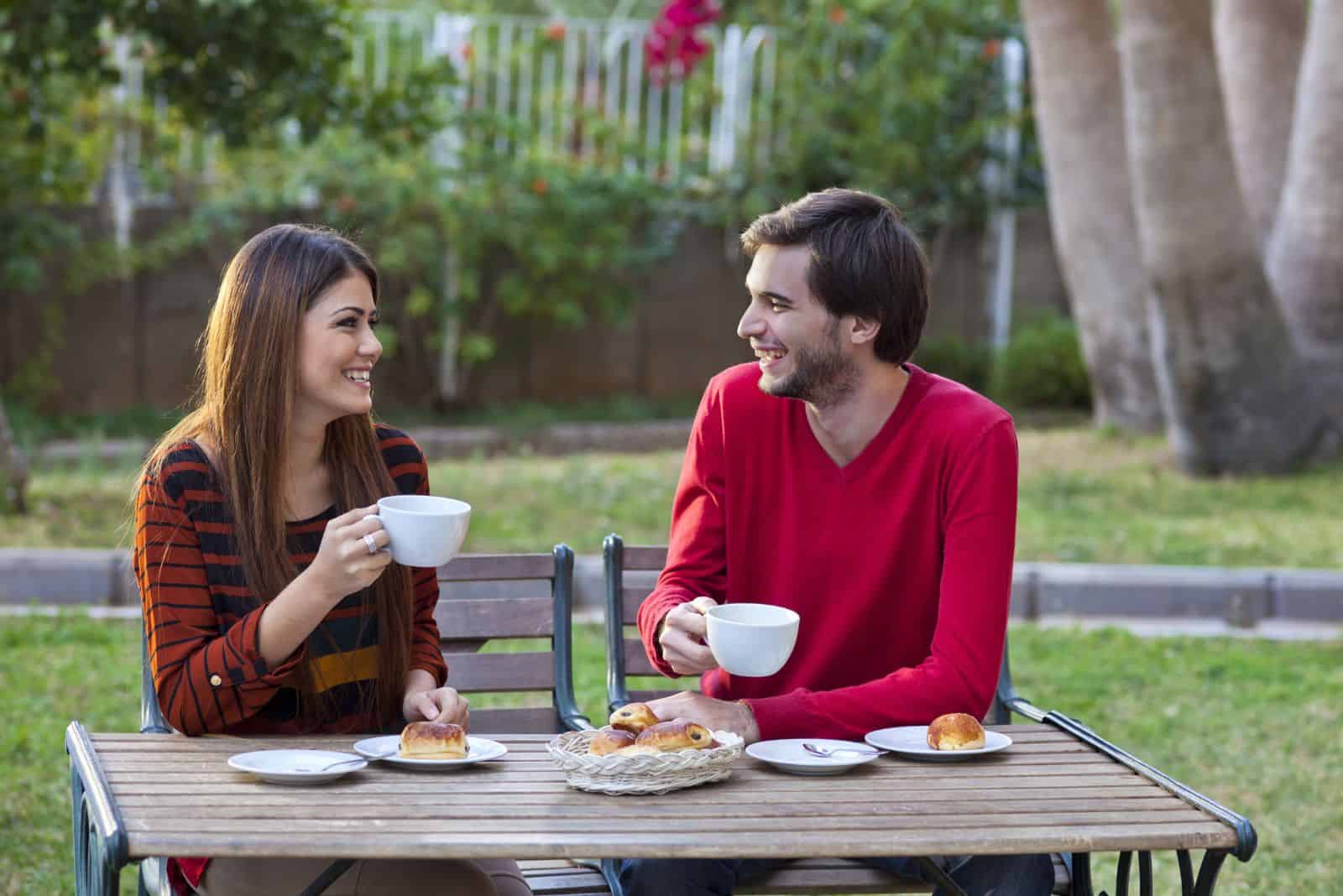 smiling man and woman are sitting in the garden having breakfast and talking