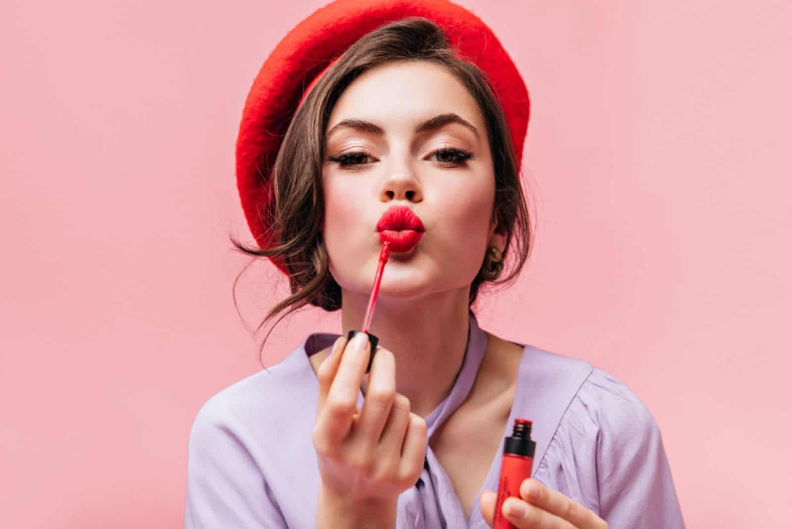  young girl in red beret painting her lips with bright lipstick 