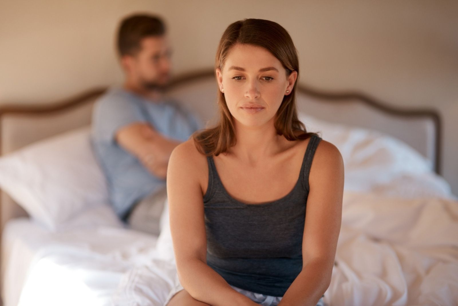 sad woman sitting on bed with man behind