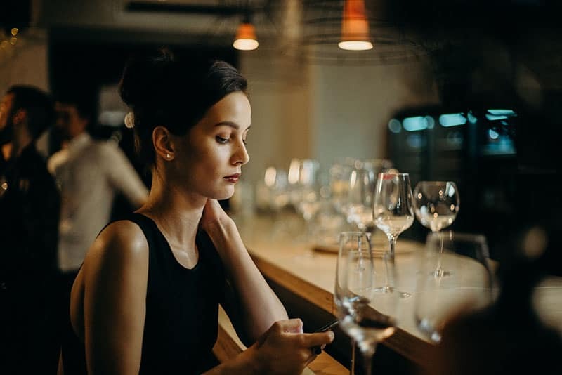 elegante mujer sentada en el bar y desplazándose en el teléfono móvil