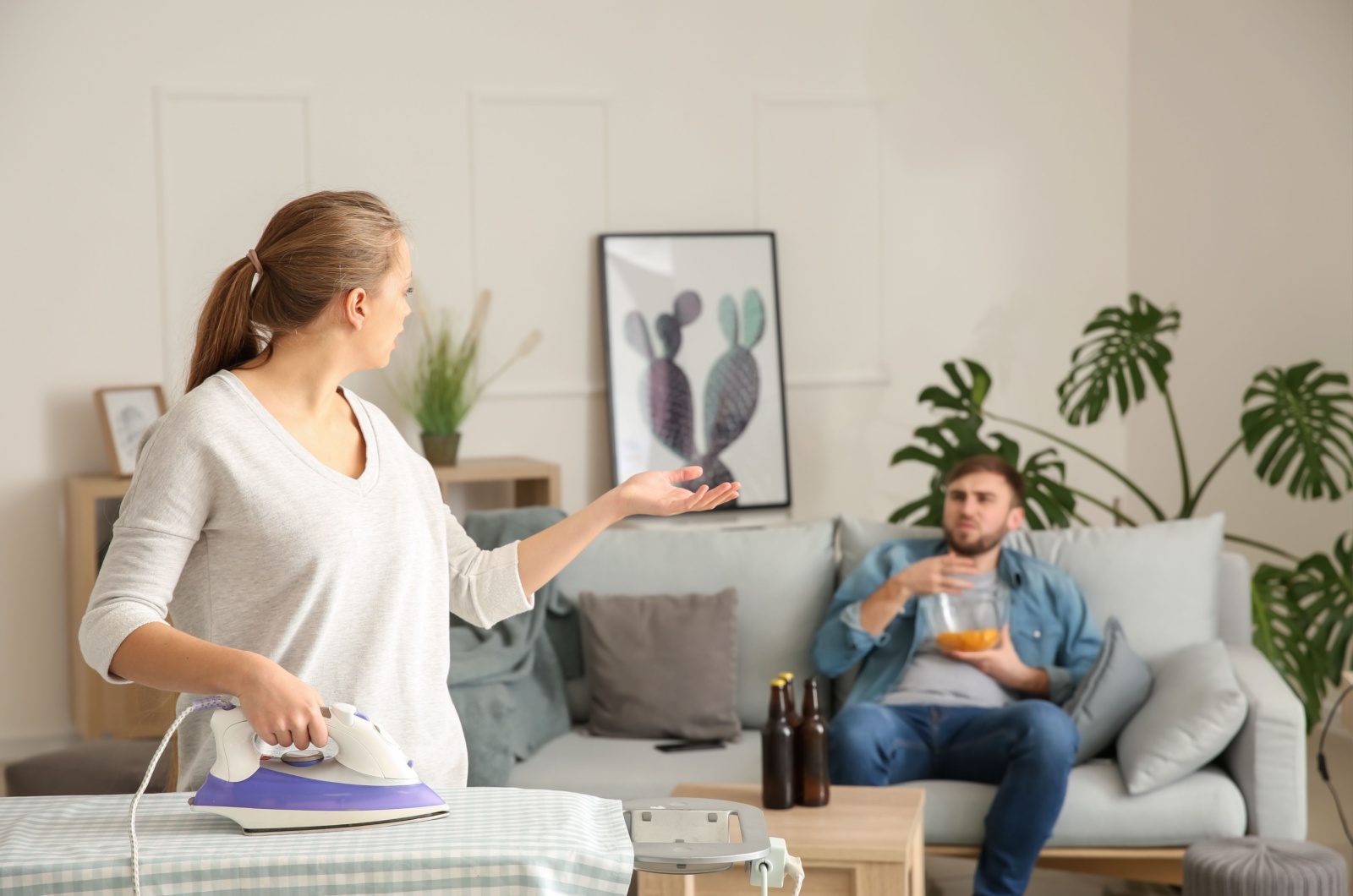 woman ironing while man sits on couch