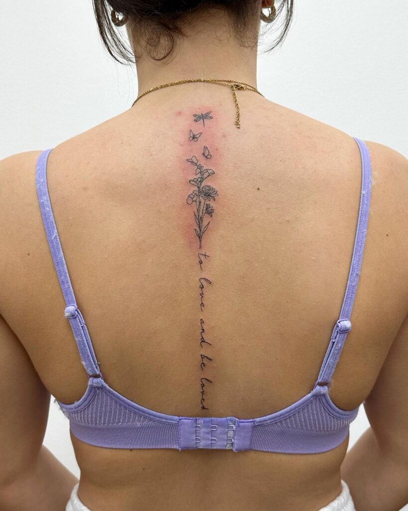 tatuaggio della colonna vertebrale con fiore, farfalla e una piccola scritta