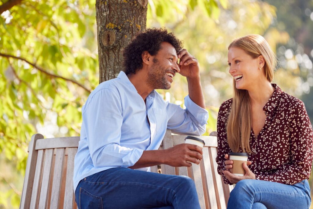 a smiling couple is sitting on a bench and talking