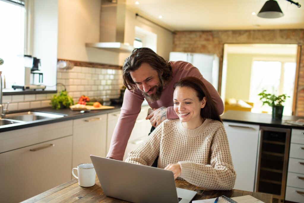 a smiling man is standing next to a woman who is behind a laptop