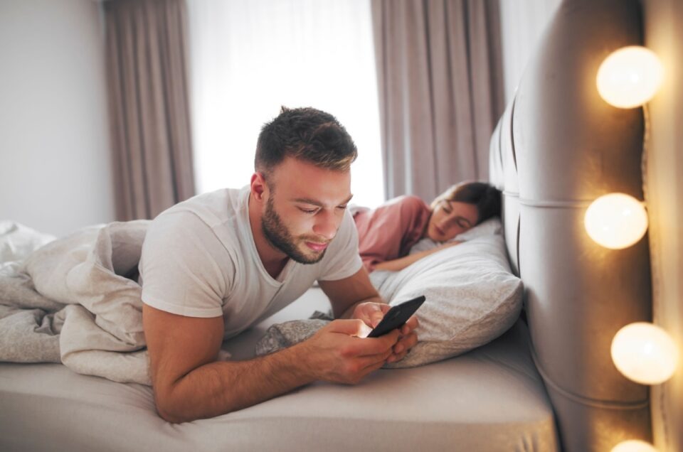 man texting wiith woman in bed