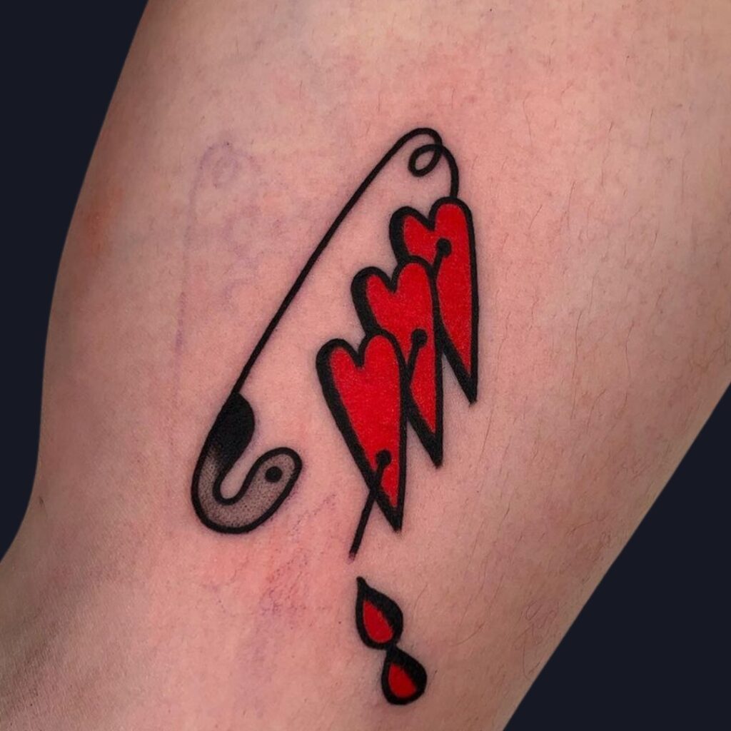 Tatuaje de imperdible y tres corazones rojos